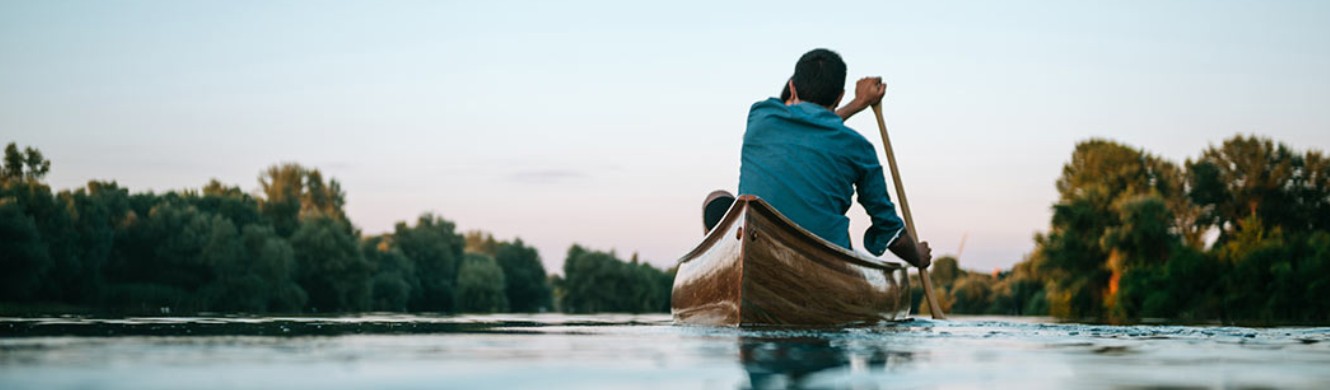 Looking at a man from behind paddling a canoe 